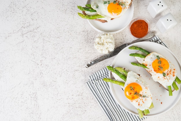 Crispy toast with cream cheese cream, fried egg and asparagus in a plate on a white background.