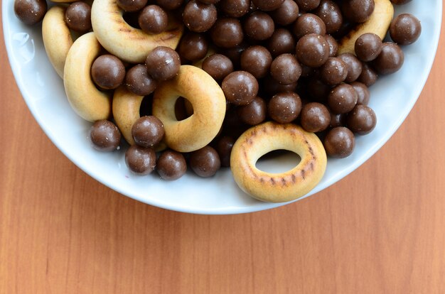 Crispy tubules, chocolate melting balls and bagels lie in a white plate on a wooden table