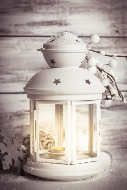 Cristmas lantern with decorations and snow over white shabby wooden background