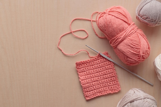 Crochet handmade square pattern pink yarn coil hook knitting crocheting top view on a wooden background