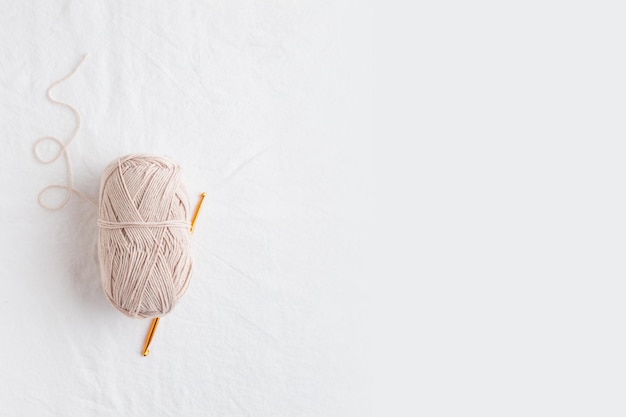 Crochet hook and ball of cotton yarn beidge color on a white table