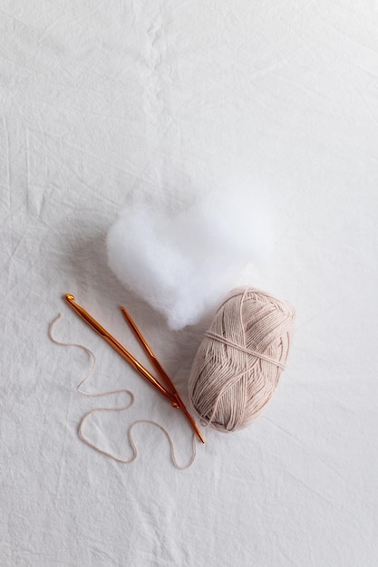 Crochet hook and ball of cotton yarn beidge color on a white table