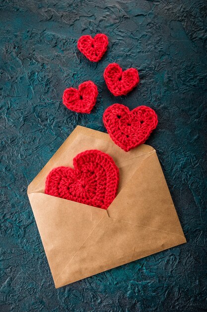 Crochet i cuori di san valentino e la busta sulla superficie scura.