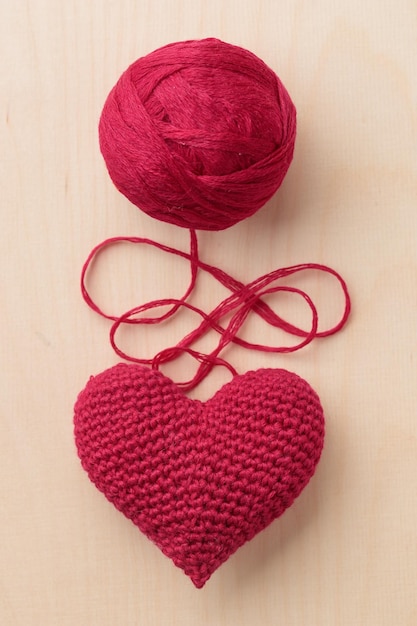 Crocheted amigurumi pink red heart on a wooden background with a skein of yarn Valentine's day