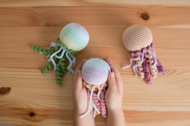 Crocheted handmade toy jellyfish in the hands of a child on a wooden background