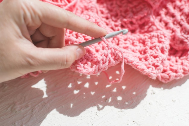 Crocheting Hobby crocheting Closeup of a metal hook and a pink skein of thread and knitted fabric