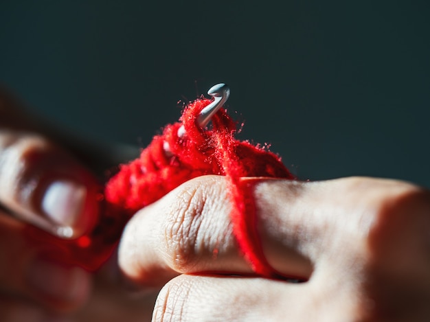 Crocheting with red wool yarn on a dark background