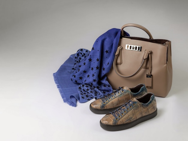 Crocodile leather sneakers next to a leather bag and a woolen scarf