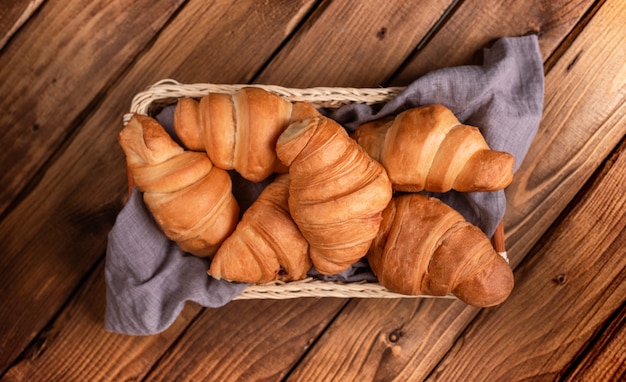 Foto croissant in un cesto su un tovagliolo grigio-blu su un tavolo di legno.