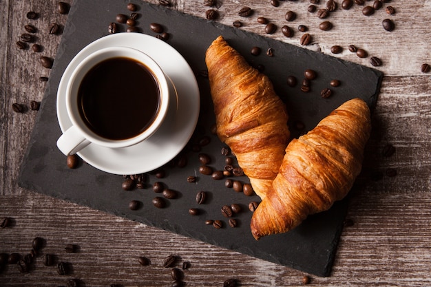 Croissant e tazza di caffè caldo sul tavolo di legno scuro. ottima colazione.