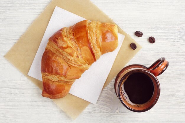 Croissant and cup of hot coffee on rustic table, top view