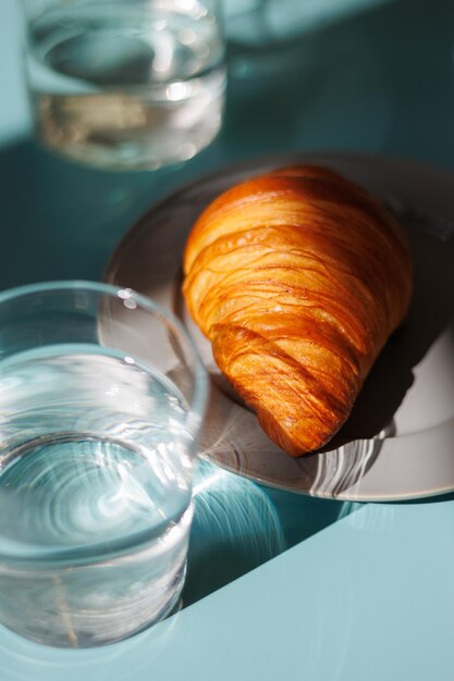 Croissant en een glas water en op blauwe tafel voor het ontbijt thuis of in het café-restaurant