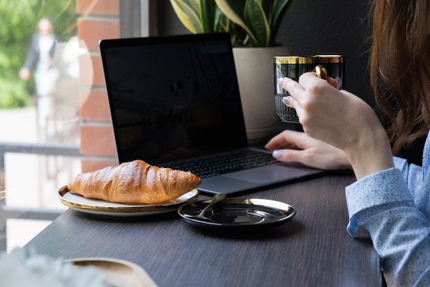 Croissant en vrouwelijke hand met kopje koffie laptop in café Freelance concept