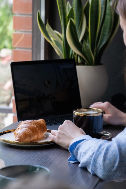 Croissant and female hand with cup of coffee laptop in cafe Freelance concept