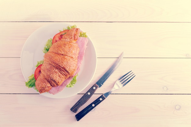 Croissant gevuld met ham en kruiden op witte houten achtergrond