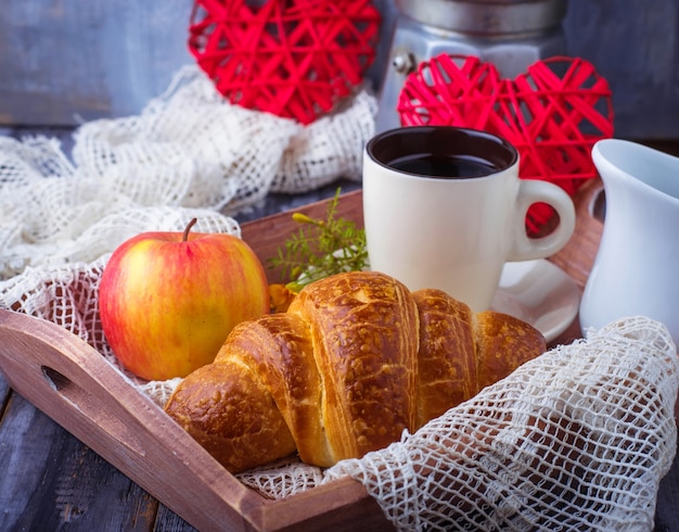 Croissant, koffie en hart op houten achtergrond