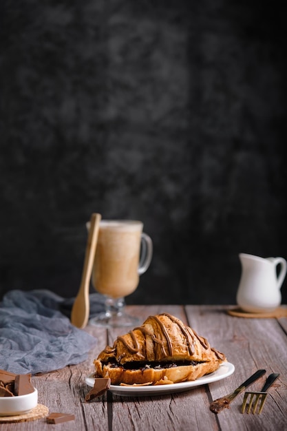 Croissant met chocolade op een houten tafel, een glaasje cappuccino of koffie, heerlijk ontbijt