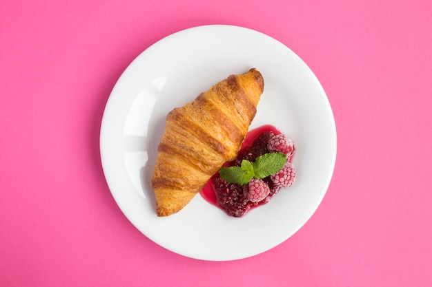 Croissant met frambozenjam in de witte plaat in het midden van de roze achtergrond. Bovenaanzicht. Ruimte kopiëren.