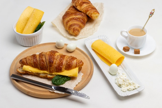 Croissant met kaas en greens, twee eieren aan boord. Kop koffie. Witte achtergrond. Bovenaanzicht