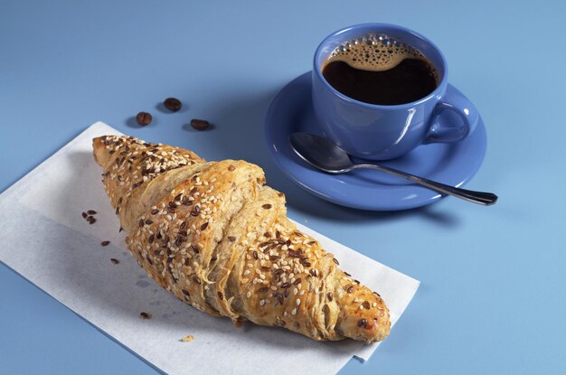 Croissant met lijnzaad en kop warme koffie voor het ontbijt op blauwe tafel