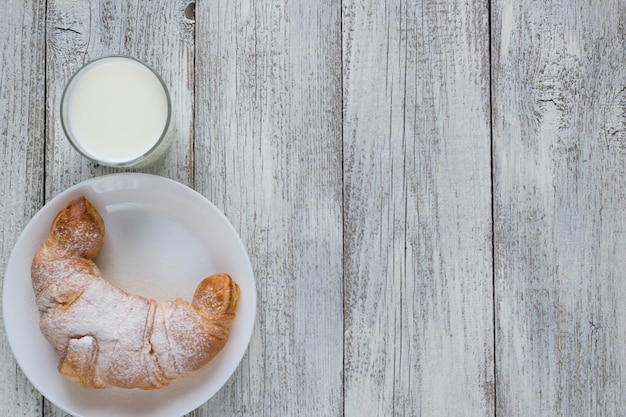 Croissant op schotel met melk op oude houten tafel voor ontbijt achtergrond.