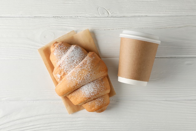 Croissant and paper cup on wooden background, space for text