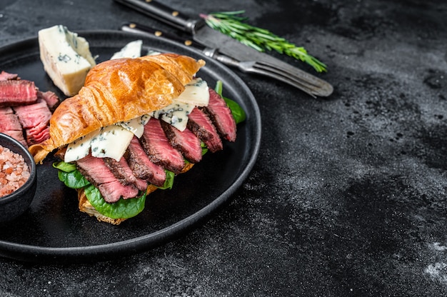 Croissant Sandwich met filet Mignon ossenhaas vlees steak met blauwe kaas. Zwarte achtergrond. Bovenaanzicht. Kopieer ruimte.