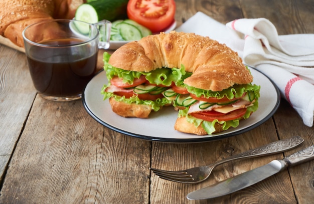 Croissant sandwich met tomaten, komkommers, spek, kaas en sla op een plaat