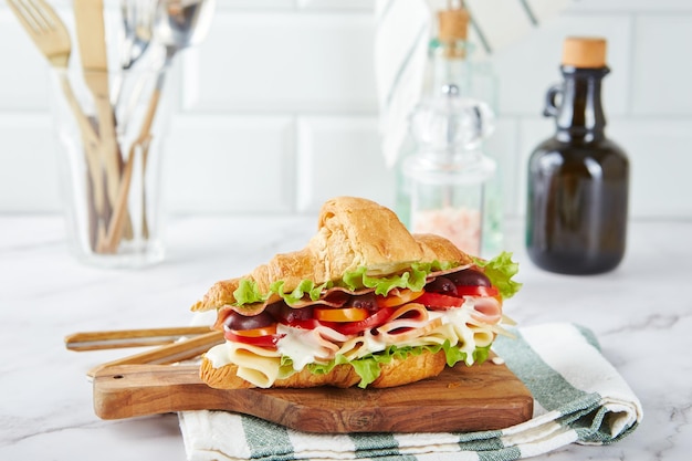 Sandwich di croissant con formaggio prosciutto lattuga pomodori olive e deliziosa salsa su tavola di legno