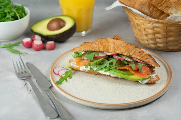 Croissant sandwich with cream cheese salmon and arugula on a white plate gray background closeup