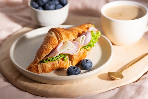 Сэндвич с кроассаном, сыром и салатами, чашка кофе, ягоды в постели, утренний завтрак.