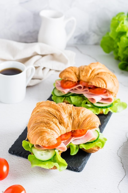 Croissant sandwiches with ham lettuce and vegetables on a slate on the table Vertical view