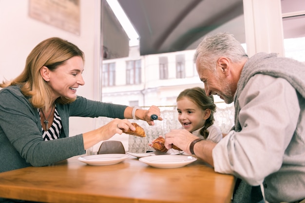 Croissant voor meisje. Liefdevolle zorgzame grootouders die hun kleine schattige mooie meid een verse croissant geven