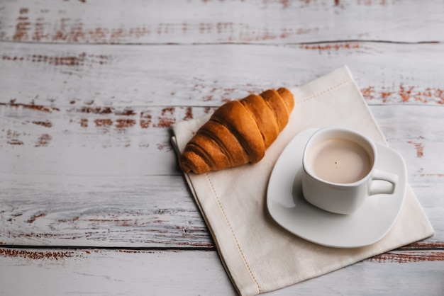 Croissant e una tazza di caffè bianca su una tavola di legno