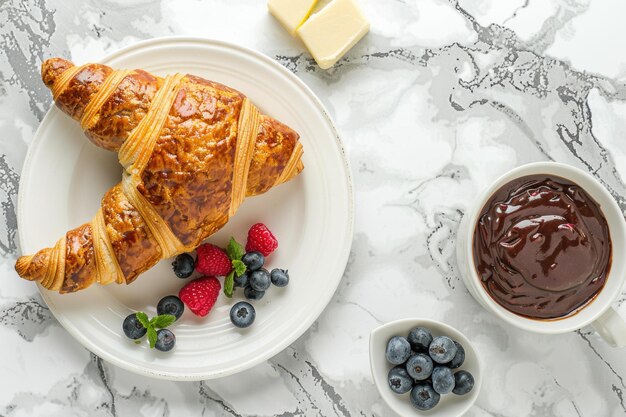 Photo croissant with berries chocolate butter coffee on marble background