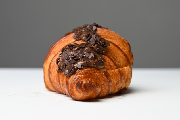 Croissant with chocolate chip topping on white table side\
view