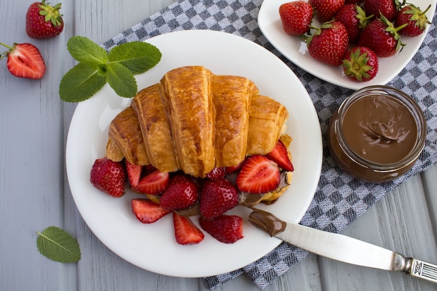 Croissant  with chocolate cream  and strawberry on the  white plate in the grey napkin.Top view.