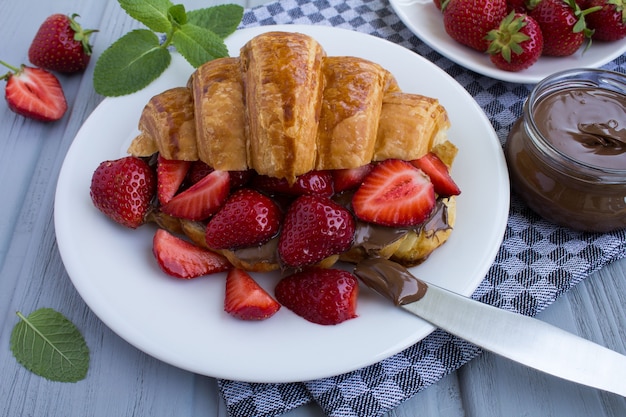 Croissant  with chocolate cream  and strawberry on the  white plate in the grey napkin