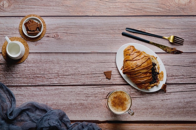 Croissant with chocolate on a wooden table, a glass of cappuccino or coffee, delicious breakfast