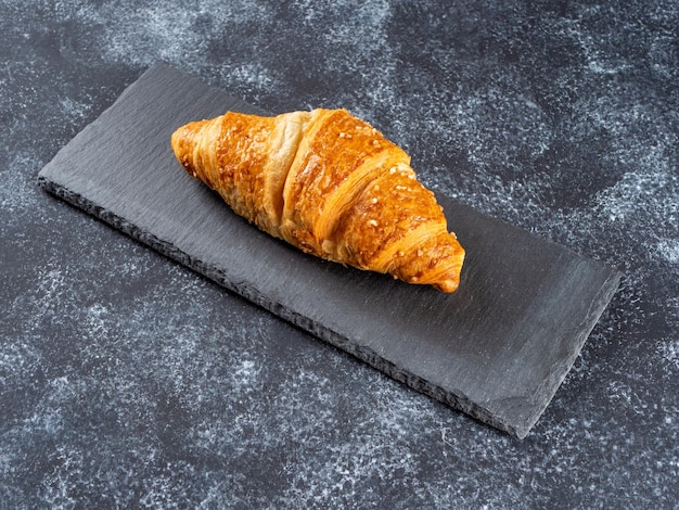 Croissant con ripieno di crema adagiato su un tagliere di ardesia su uno sfondo scuro