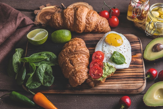 Croissant with guacamole avocado, fried egg and tomato, spinach leaves