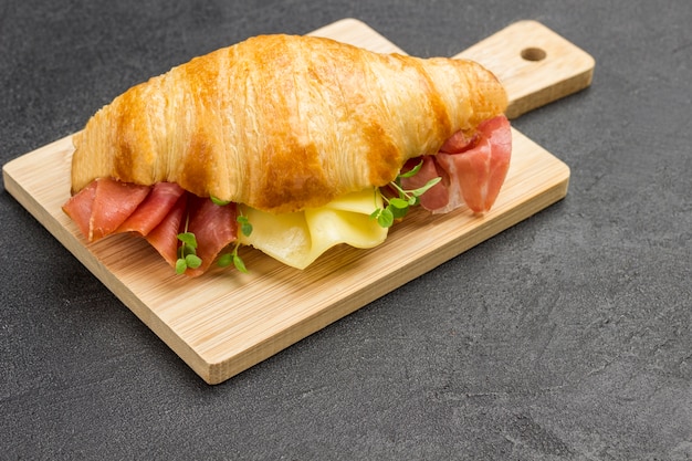 Croissant with jamon and cheese and greens on cutting board. Copy space. Black surface.