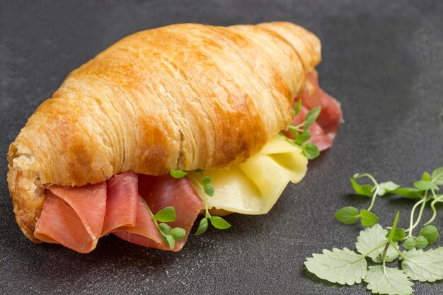 Foto croissant con prosciutto e formaggio verdi sul tavolo sfondio nero