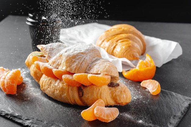 Photo croissant with mandarins sweet on a dark background homemade croissants falling powdered sugar verti