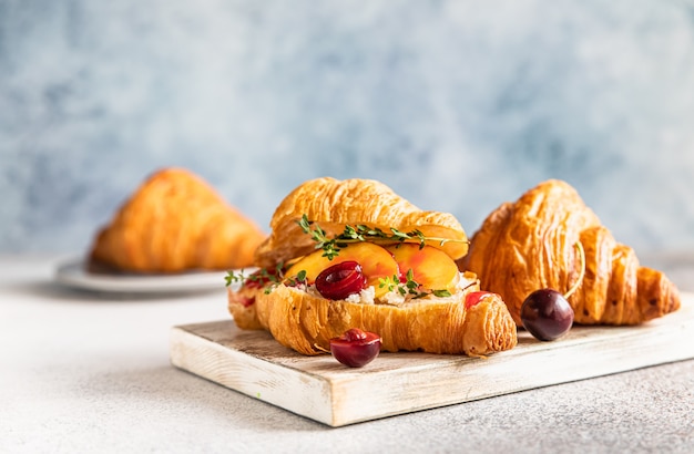 Photo croissant with nectarine, cherry and ricotta or cream cheese on wooden cutting board.