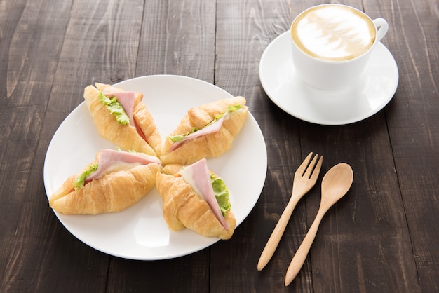 Croissant with parma ham and coffee on wooden table