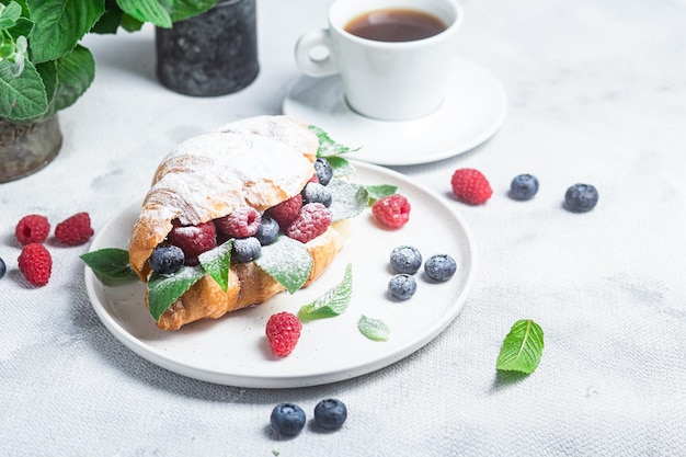 Croissant with raspberries blueberries and cream cheese on a white plate