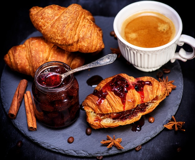 Croissant with strawberry jam and white cup with coffee 