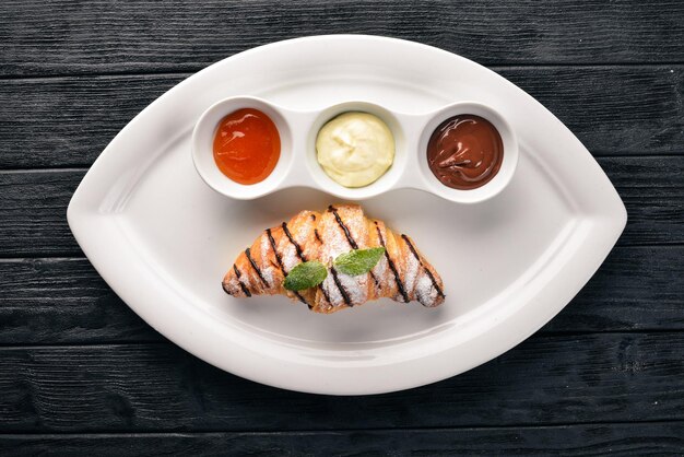 Croissant with sweet sauces Chocolate Vanilla and Peach On a wooden background Top view
