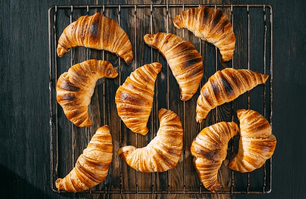 Croissants on a baking rack cool after baking on a dark wooden table
